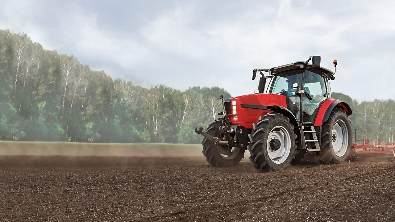  A red tractor ploughing a muddy field with trees in the background