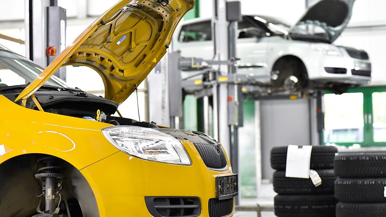 two cars in a garage, one yellow and one white, with their bonnets open, and some car tyres in the background
