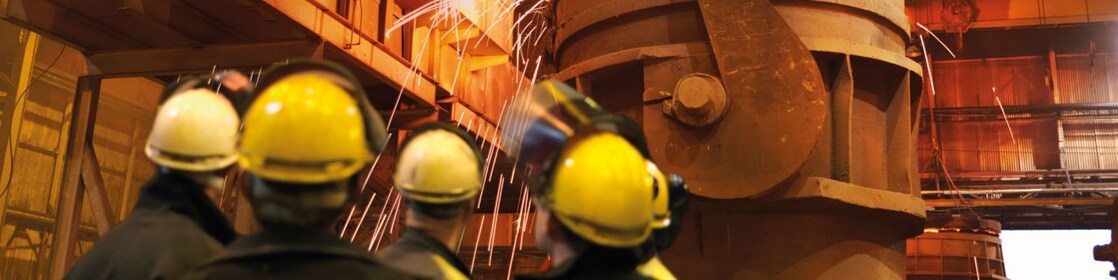 trabajadores mirando maquinaria pesada en una planta de procesamiento de metales