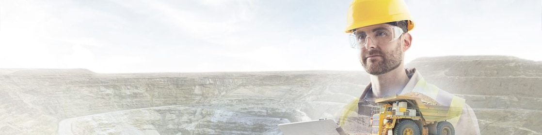 worker in yellow hard hat transposed onto a background of cliffs and a large yellow truck