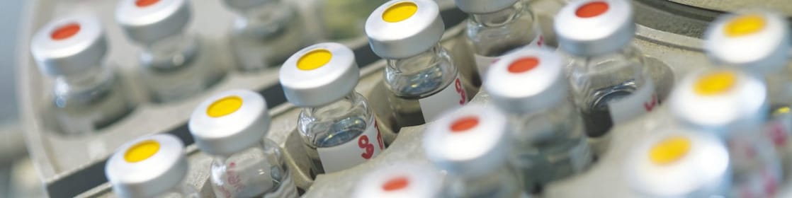 Filas de frascos de medicamentos en un soporte, algunas de ellas con puntos rojos y otras con puntos amarillos en la tapa