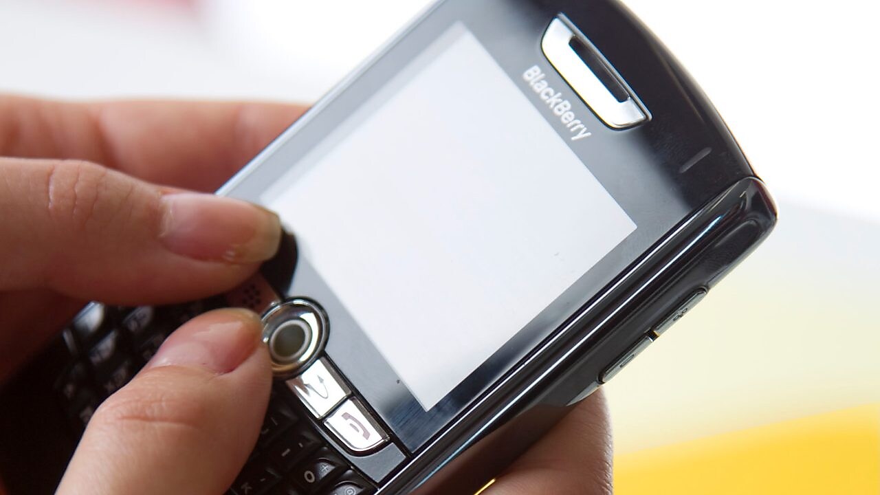 Se ven dos manos usando un dispositivo blackberry para enviar un mensaje electrónico