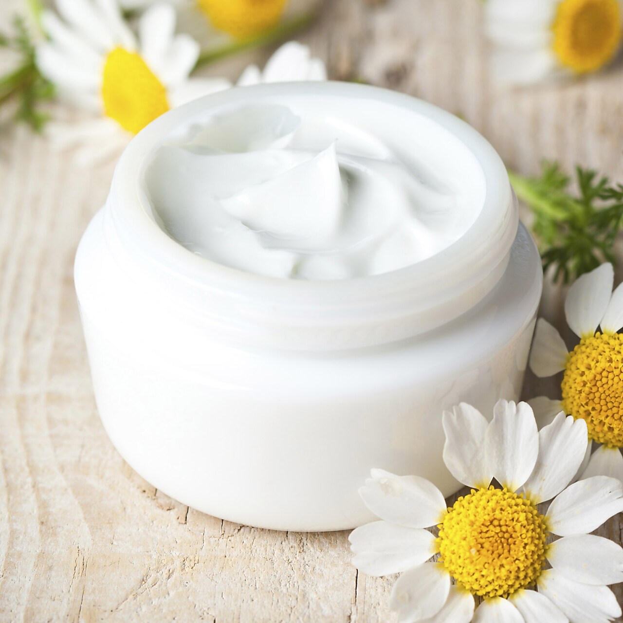 Un pote de crema facial blanca en una mesa rodeada de flores