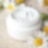 Un pote de crema facial blanca en una mesa rodeada de flores