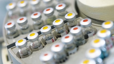 Filas de frascos de medicamentos en un soporte, algunas de ellas con puntos rojos y otras con puntos amarillos en la tapa