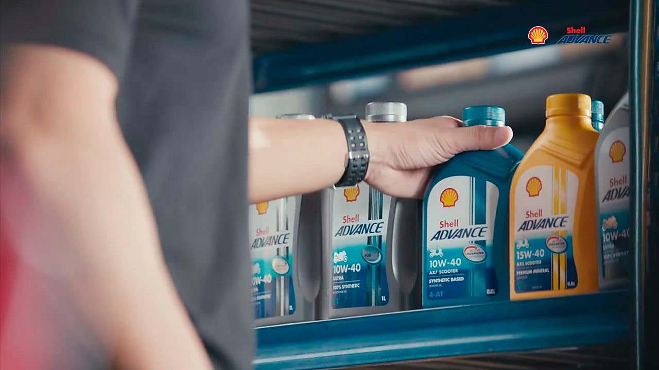 Mano tocando las botellas de Shell Advance en un estante