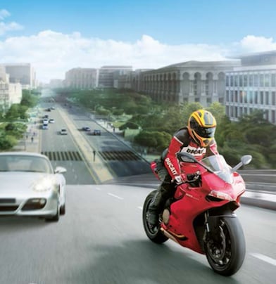 Motocicleta roja y piloto en una ruta con autos y edificios en el fondo