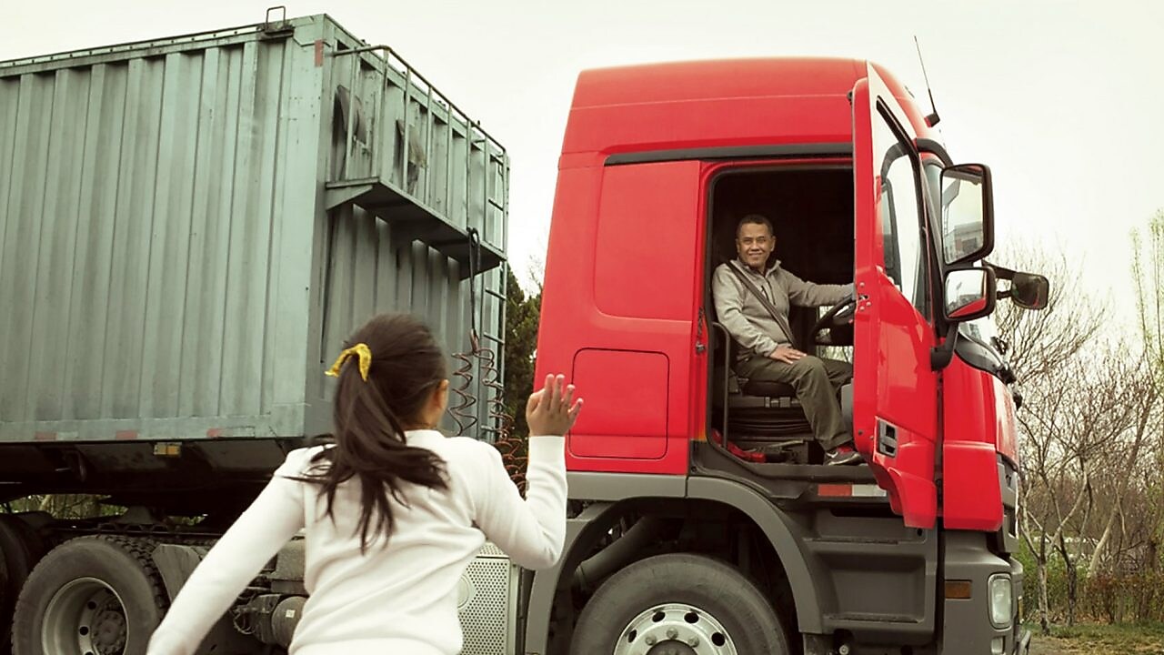 Hombre en una cabina roja de camión con la puerta abierta despidiéndose de su hija