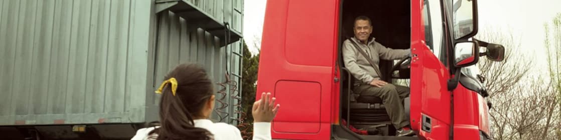 Hombre en una cabina roja de camión con la puerta abierta despidiéndose de su hija