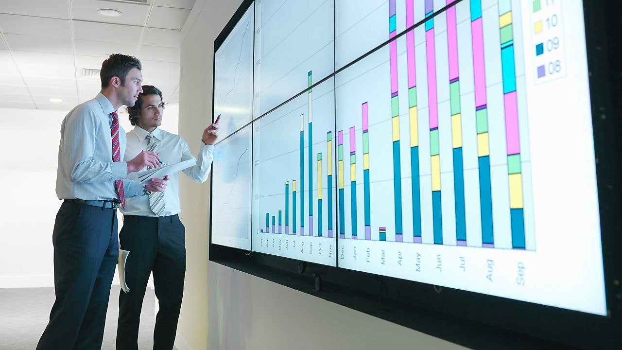 Hombres de negocios analizan informes visualizados en una gran pantalla digital